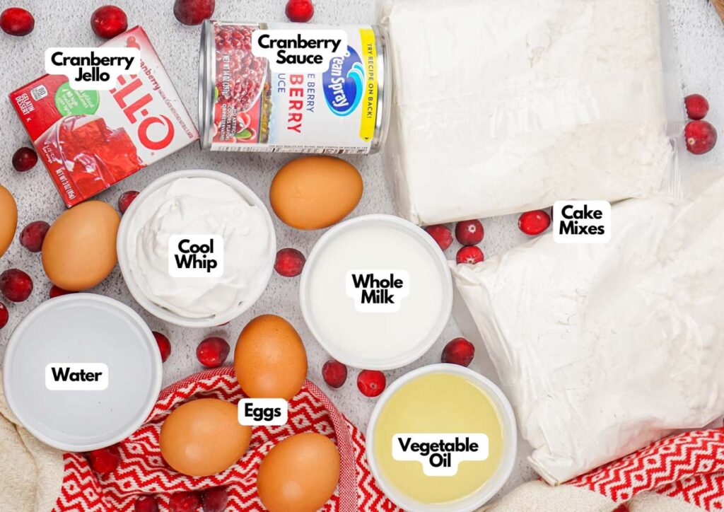 Ingredients for a festive Christmas Poke Cake, including cranberry Jello, cranberry sauce, cake mixes, Cool Whip, whole milk, eggs, water, and vegetable oil, are arranged on a surface with cranberries.