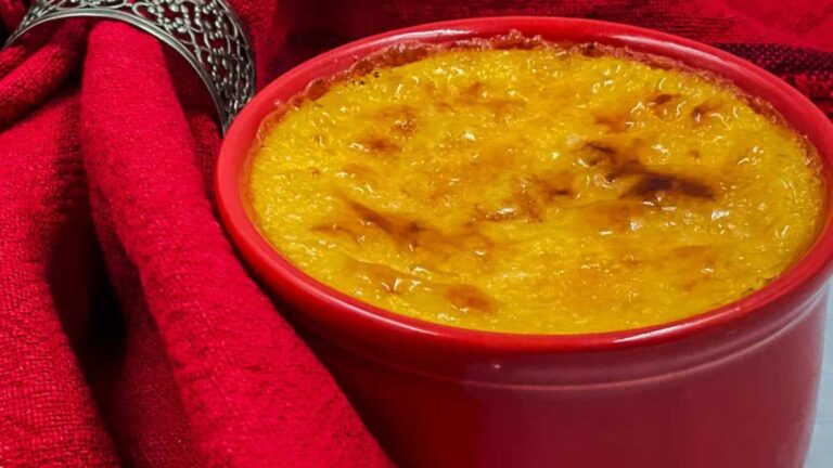 A red ramekin filled with creme brulee is placed beside a red cloth napkin with a silver napkin ring.