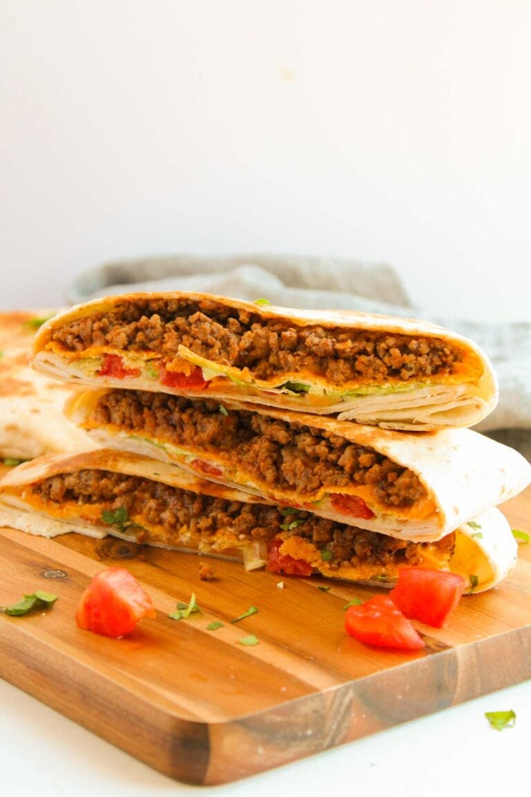Three halved beef and cheese quesadillas with diced tomatoes and herbs are stacked on a wooden board.