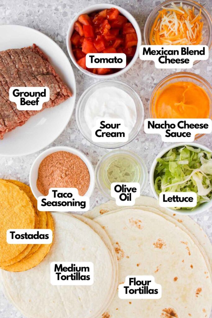 Ingredients arranged for taco preparation, including ground beef, tomato, Mexican blend cheese, nacho cheese sauce, sour cream, taco seasoning, olive oil, lettuce, tostadas, and tortillas.