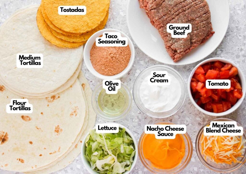 Ingredients for homemade Crunchwrap Supreme laid out on a gray surface, including ground beef, flour tortillas, tostadas, taco seasoning, nacho cheese sauce, sour cream, lettuce, tomato, Mexican blend cheese, and olive oil.