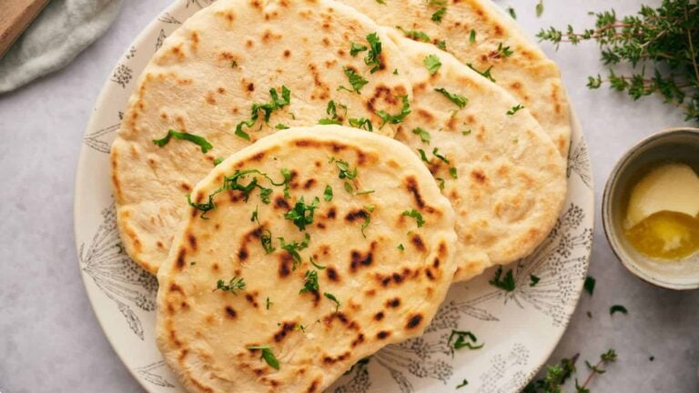A plate of naan bread garnished with chopped herbs, next to a small bowl of melted butter.