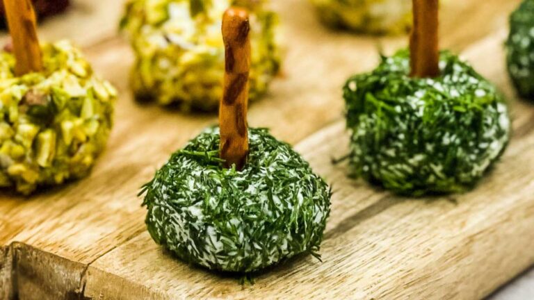 Herb-coated cheese balls with pretzel sticks on a wooden board.