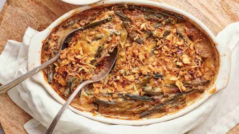 A baked casserole dish with green beans, a creamy sauce, and a crispy topping, served with two spoons on a wooden surface.
