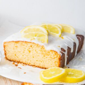A delicious lemon yogurt loaf topped with white icing and adorned with fresh lemon slices rests elegantly on parchment paper.