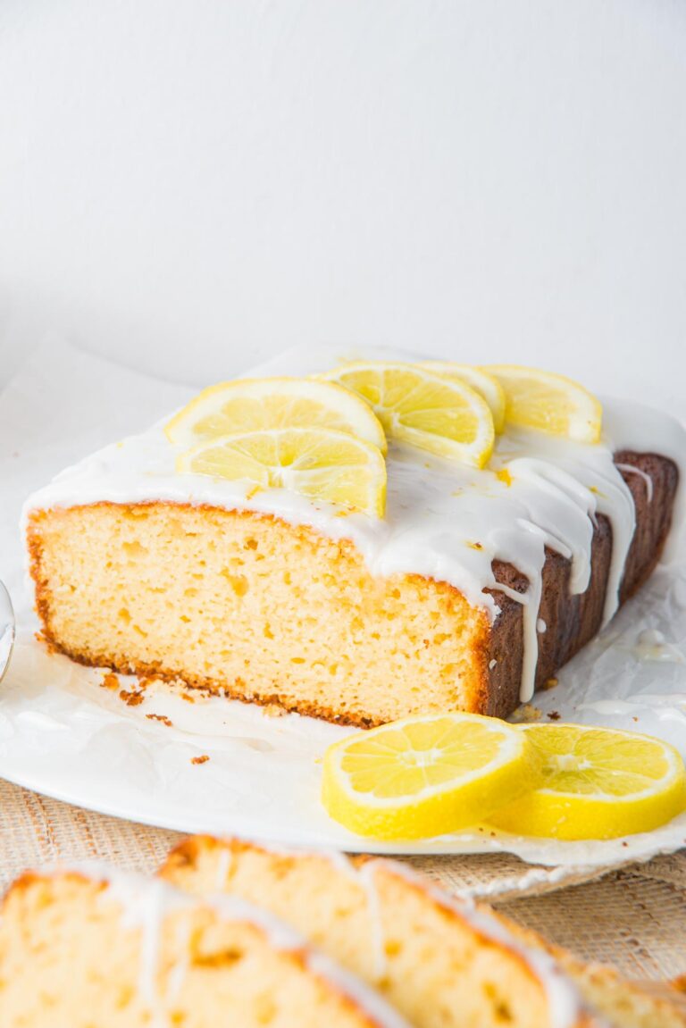 A delicious lemon yogurt loaf topped with white icing and adorned with fresh lemon slices rests elegantly on parchment paper.