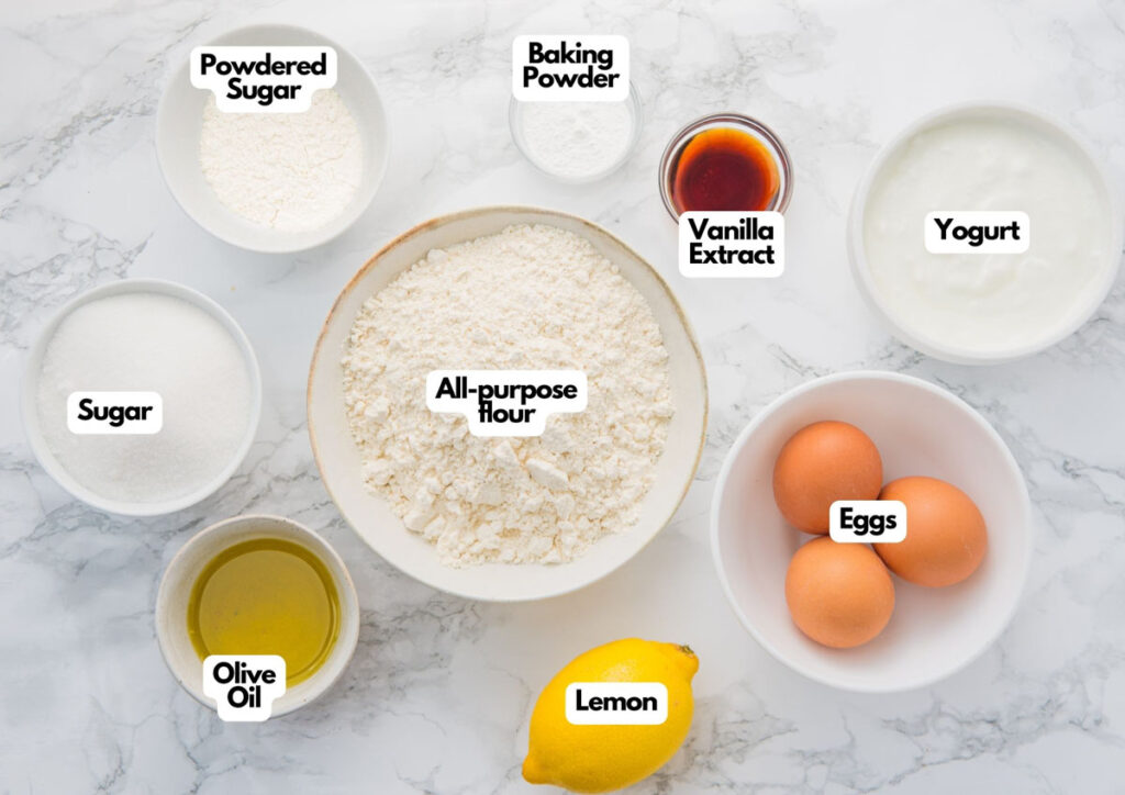Baking ingredients for a delicious lemon yogurt loaf—like all-purpose flour, sugar, powdered sugar, baking powder, vanilla extract, yogurt, eggs, olive oil, and a fresh lemon—arranged on a white marble surface.