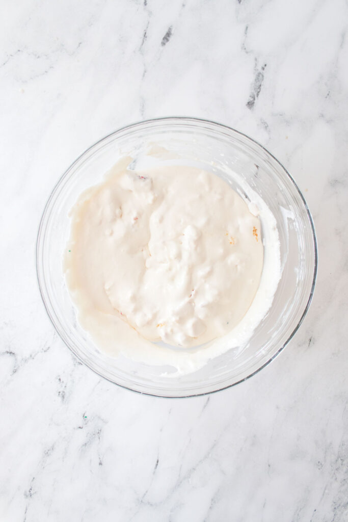 A glass bowl of creamy white batter reminiscent of a Little Debbie Christmas Tree Dip sits elegantly on a marbled surface.