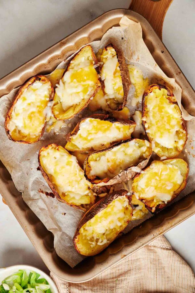 Loaded potato skins topped with melted cheese are perfectly arranged on a parchment-lined baking tray.