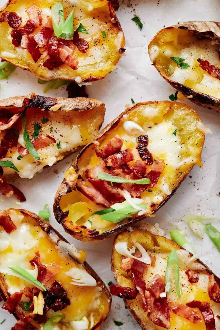Loaded potato skins topped with melted cheese, crispy bacon bits, and sliced green onions rest on a parchment-lined surface.