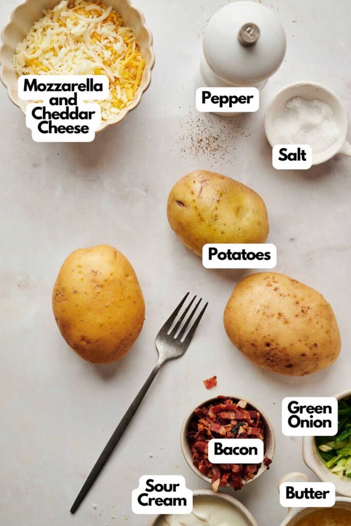 Ingredients for loaded potato skins labeled: mozzarella and cheddar cheese, pepper, salt, potatoes, sour cream, bacon, green onion, and butter. A fork lies nearby, ready to dive into the cheesy goodness.