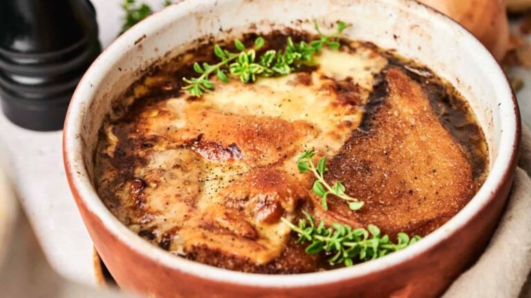 A bowl of French onion soup topped with melted cheese and garnished with sprigs of thyme.