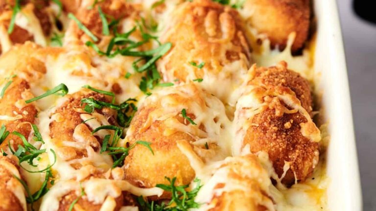 A baked dish of golden brown, cheese-covered, breaded stuffed chicken rolls garnished with chopped parsley.