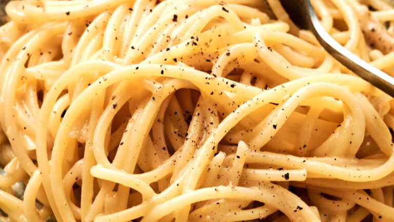 Close-up of cooked spaghetti with a sprinkle of black pepper and a fork on the right.