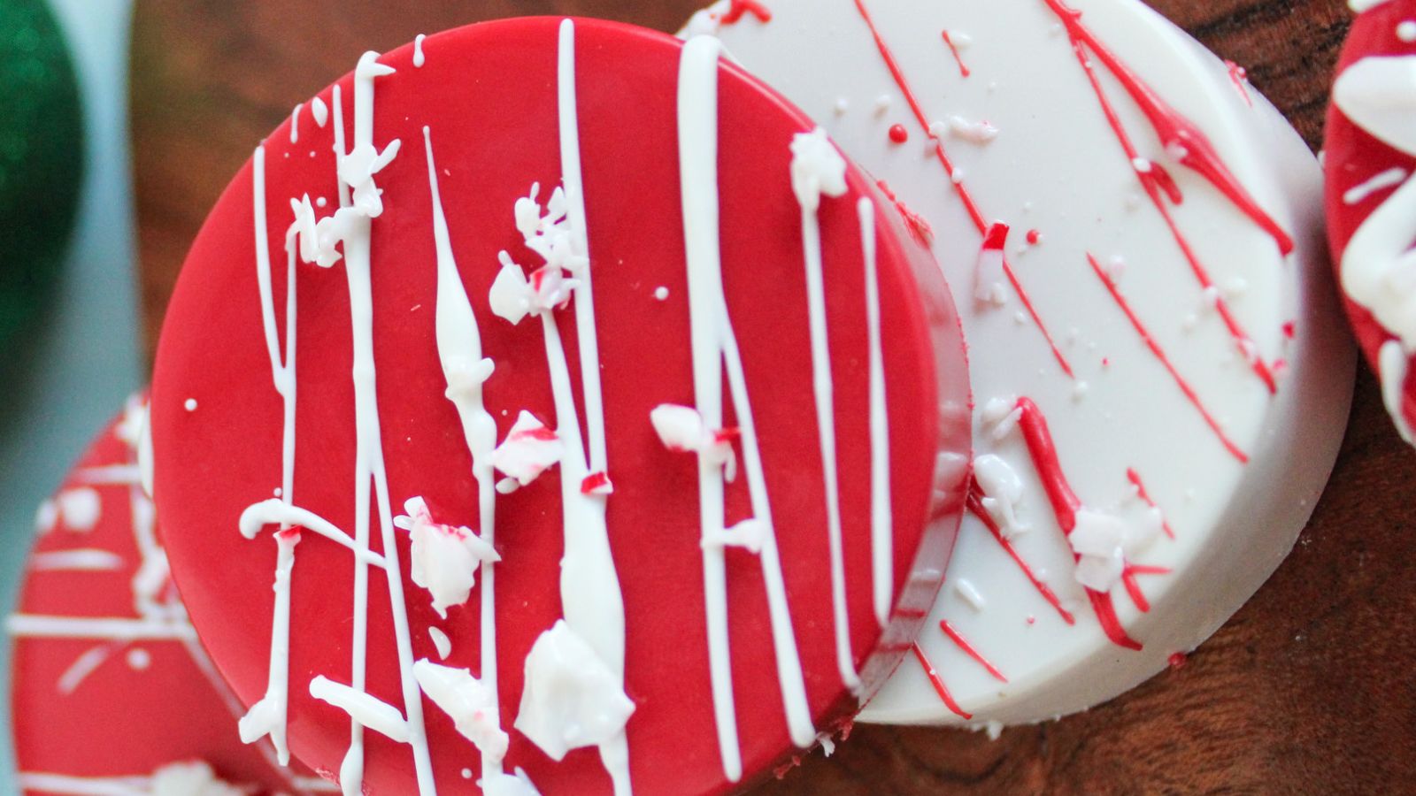 Two round cookies, one red and one white, are decorated with white icing drizzles and white sprinkles, placed on a wooden surface.