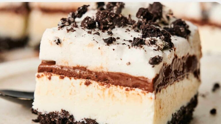 A slice of layered dessert with cream, chocolate filling, and a crumbly chocolate topping on a plate.