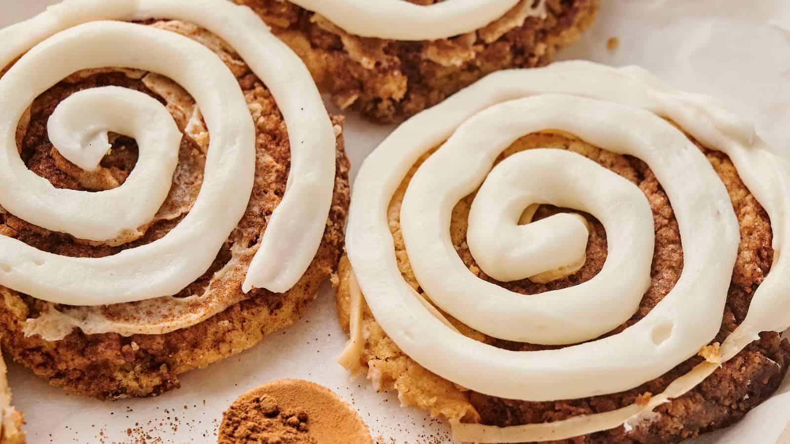 A delectable close-up of Copycat Crumbl Cinnamon Swirl Cookies, adorned with spiral white icing on a parchment paper background.