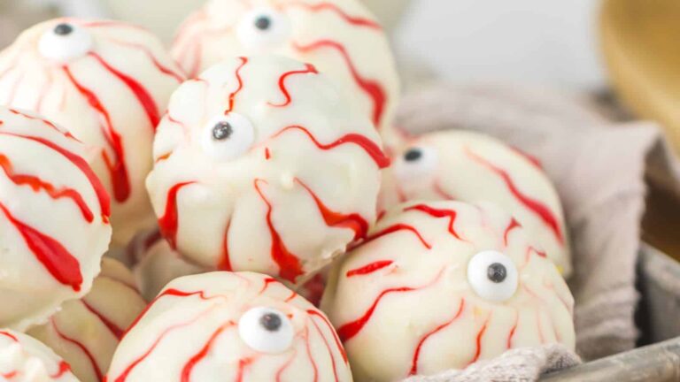 Close-up of white chocolate truffles decorated to resemble eyeballs with red icing lines and a candy to mimic a pupil.