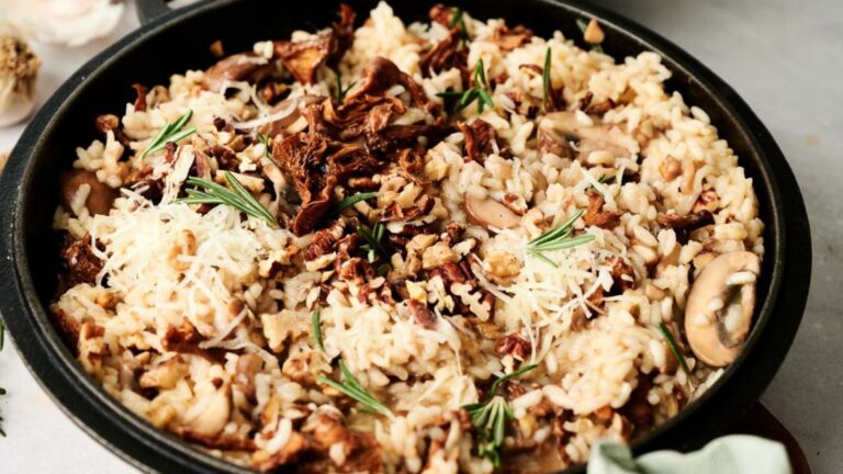 A pan of risotto with mushrooms, pecans, and rosemary, topped with grated cheese.