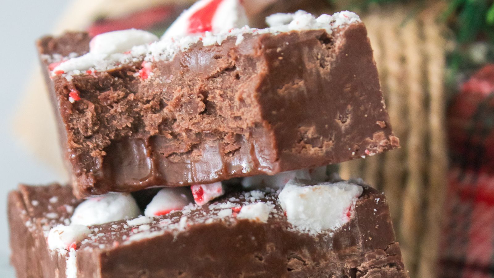Close-up of two stacked pieces of chocolate peppermint fudge, with visible crushed peppermint candy on top.