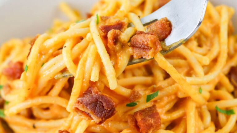 Close-up of spaghetti carbonara on a fork, with creamy sauce, crispy bacon pieces, and garnished with parsley.
