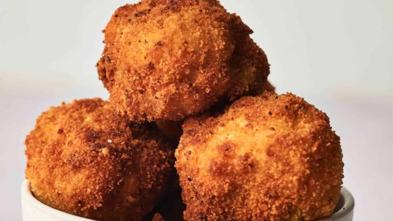 A close-up of a bowl filled with golden-brown, crispy breaded balls, suggesting a savory fried dish.