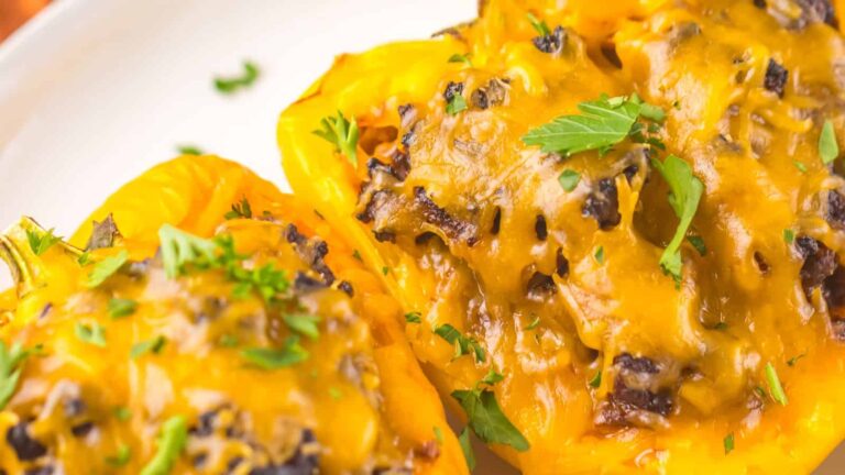 Close-up of stuffed yellow bell peppers topped with melted cheese and garnished with chopped herbs.