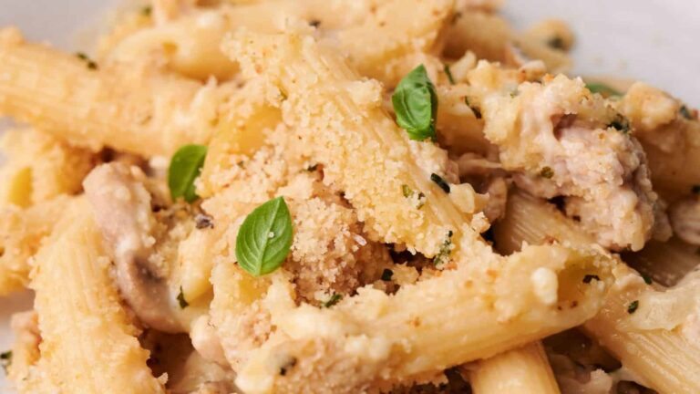 Close-up of creamy pasta with breadcrumbs, mushrooms, and small basil leaves.