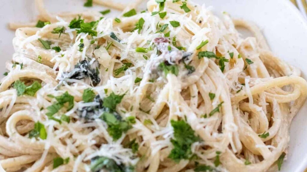 A plate of creamy spaghetti topped with chopped parsley and grated cheese.