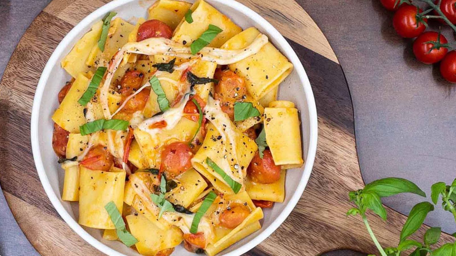 Pasta in a bowl with cheese, tomatoes, and fresh basil.