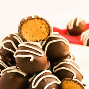 A stack of chocolate truffles drizzled with white icing, resembling decadent peanut butter balls, with one truffle cut in half to reveal its rich peanut butter filling.