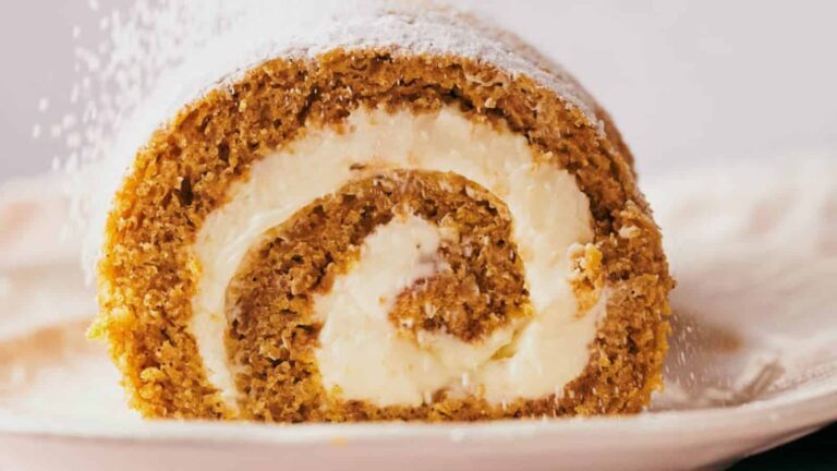 Close-up of a pumpkin roll cake with cream cheese filling, dusted with powdered sugar.