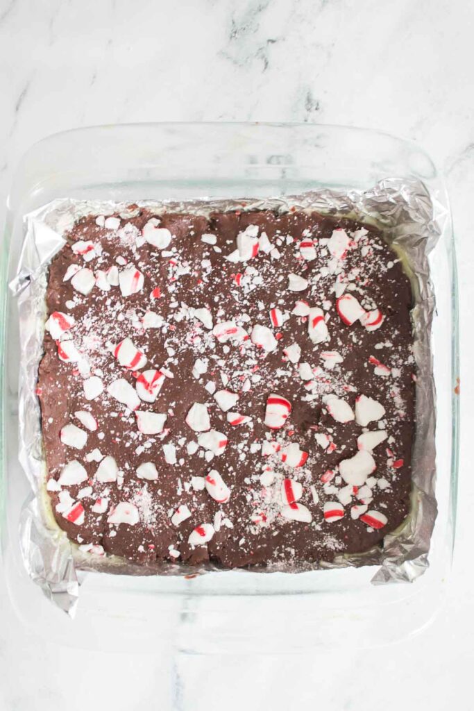 A square glass dish holds a delectable peppermint fudge dessert, crowned with crushed peppermint candies on foil.