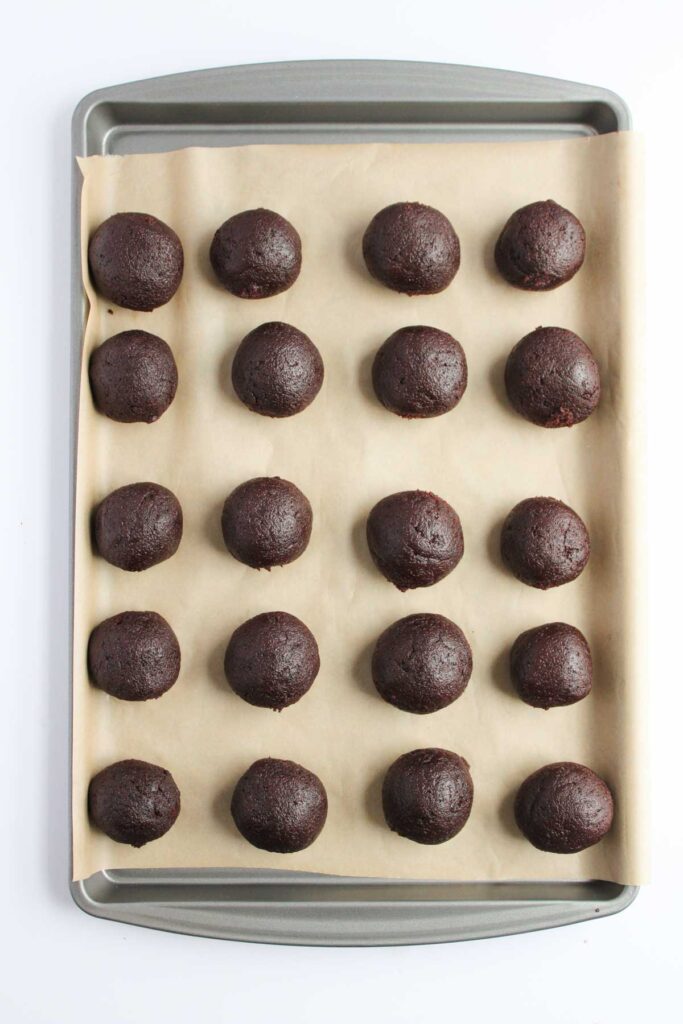 Reindeer cake pops and cookie dough balls are arranged in tidy rows on a parchment-lined baking sheet, ready for the oven's magic.