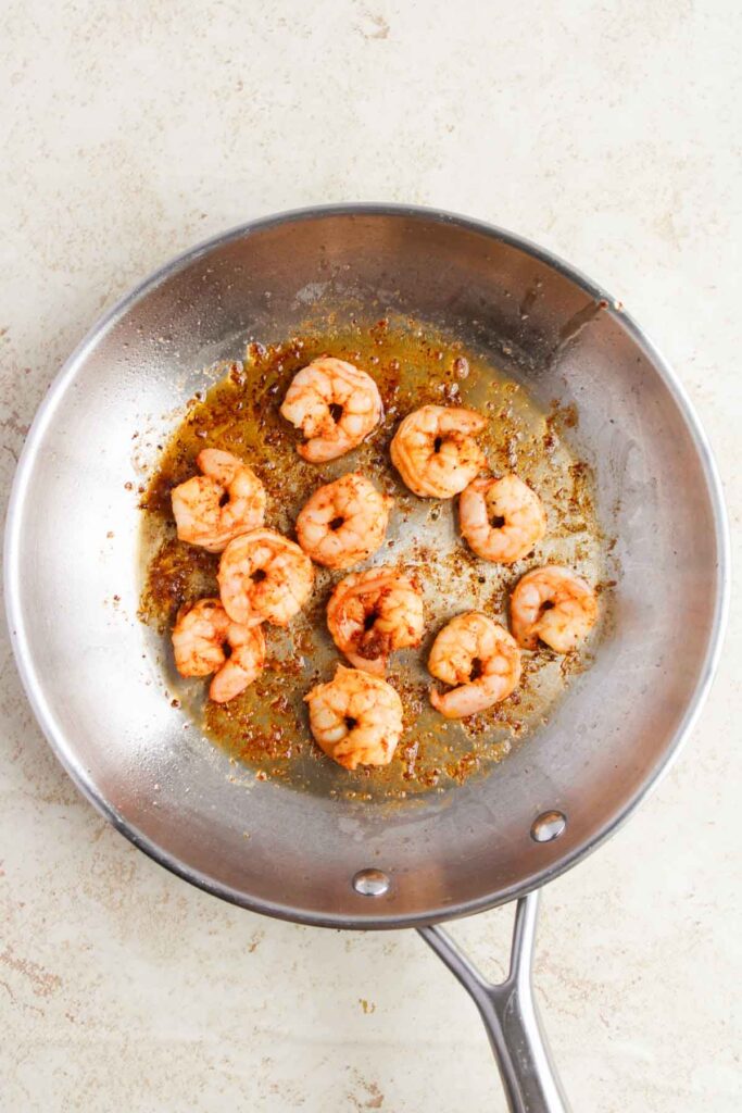 Shrimp cooking in a stainless steel pan with a light brown sauce.