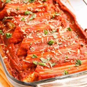 Three cheese manicotti pasta in a glass dish, generously topped with tomato sauce, grated cheese, and fresh basil.