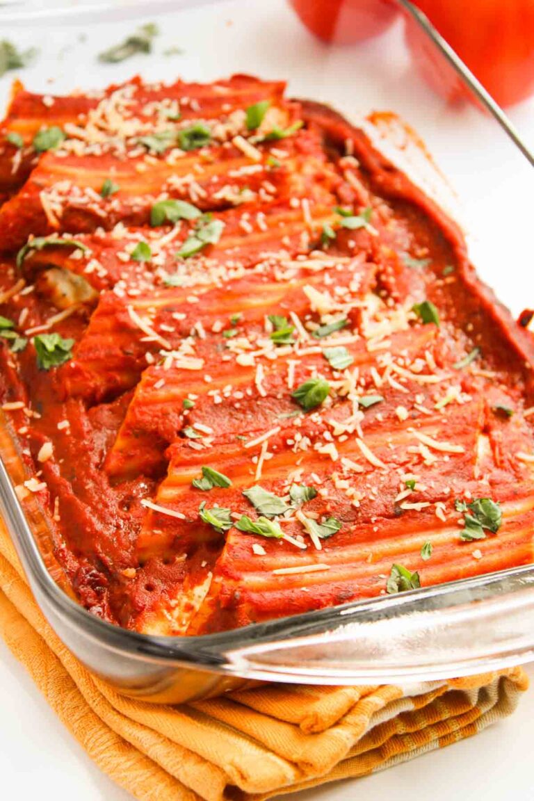 Three cheese manicotti pasta in a glass dish, generously topped with tomato sauce, grated cheese, and fresh basil.
