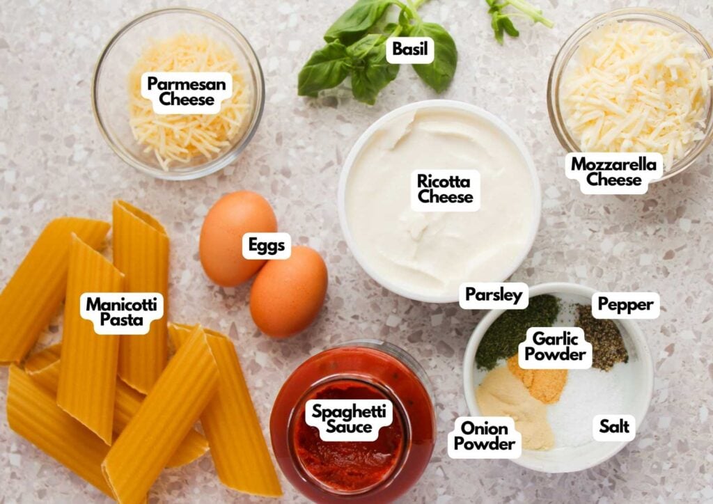 Three Cheese Manicotti ingredients—manicotti pasta, eggs, spaghetti sauce, ricotta, mozzarella, parmesan cheeses, basil, parsley, garlic powder, onion powder, salt, and pepper—are arranged on a countertop.