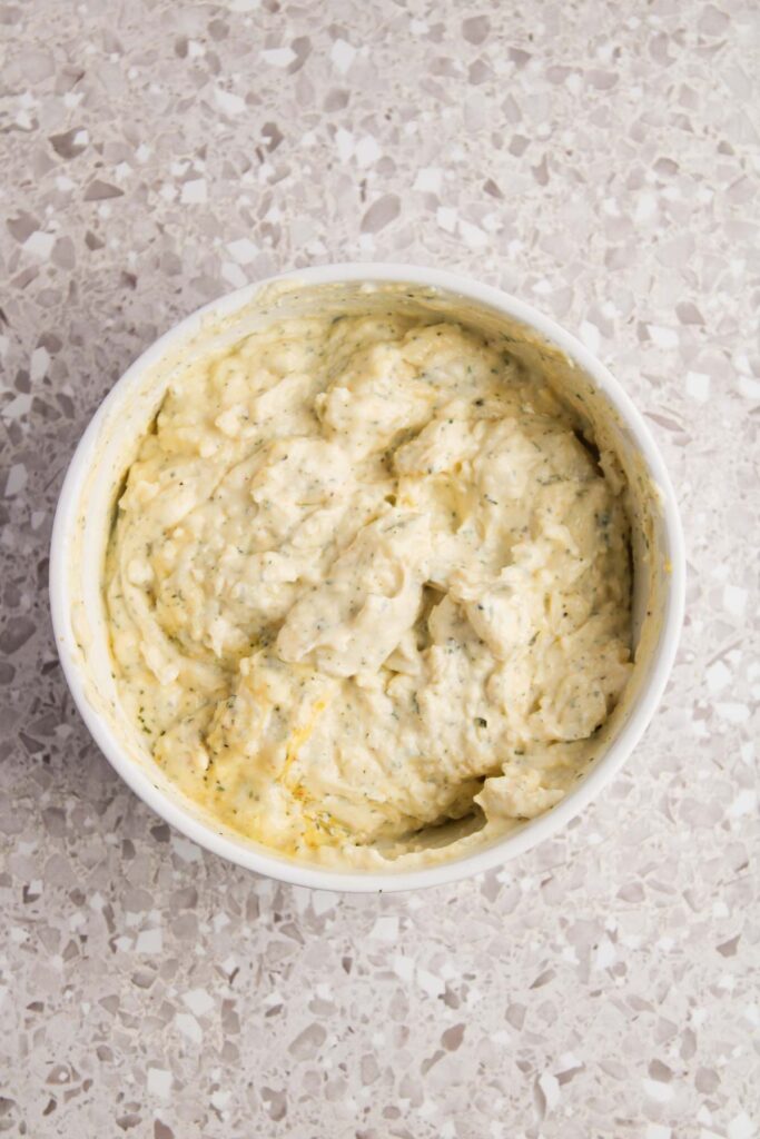 A bowl of creamy, textured Three Cheese Manicotti dip sits on a speckled countertop.