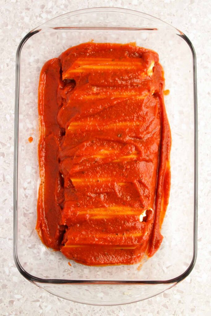 A glass baking dish cradles a delectable Three Cheese Manicotti, each piece generously stuffed and smothered in rich tomato sauce.