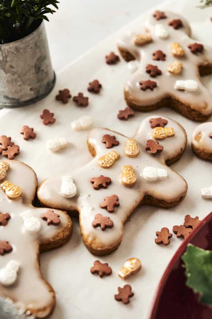 Iced gingerbread cookies shaped like people, decorated with small sugar shapes, are displayed on a white surface with scattered mini cookies.