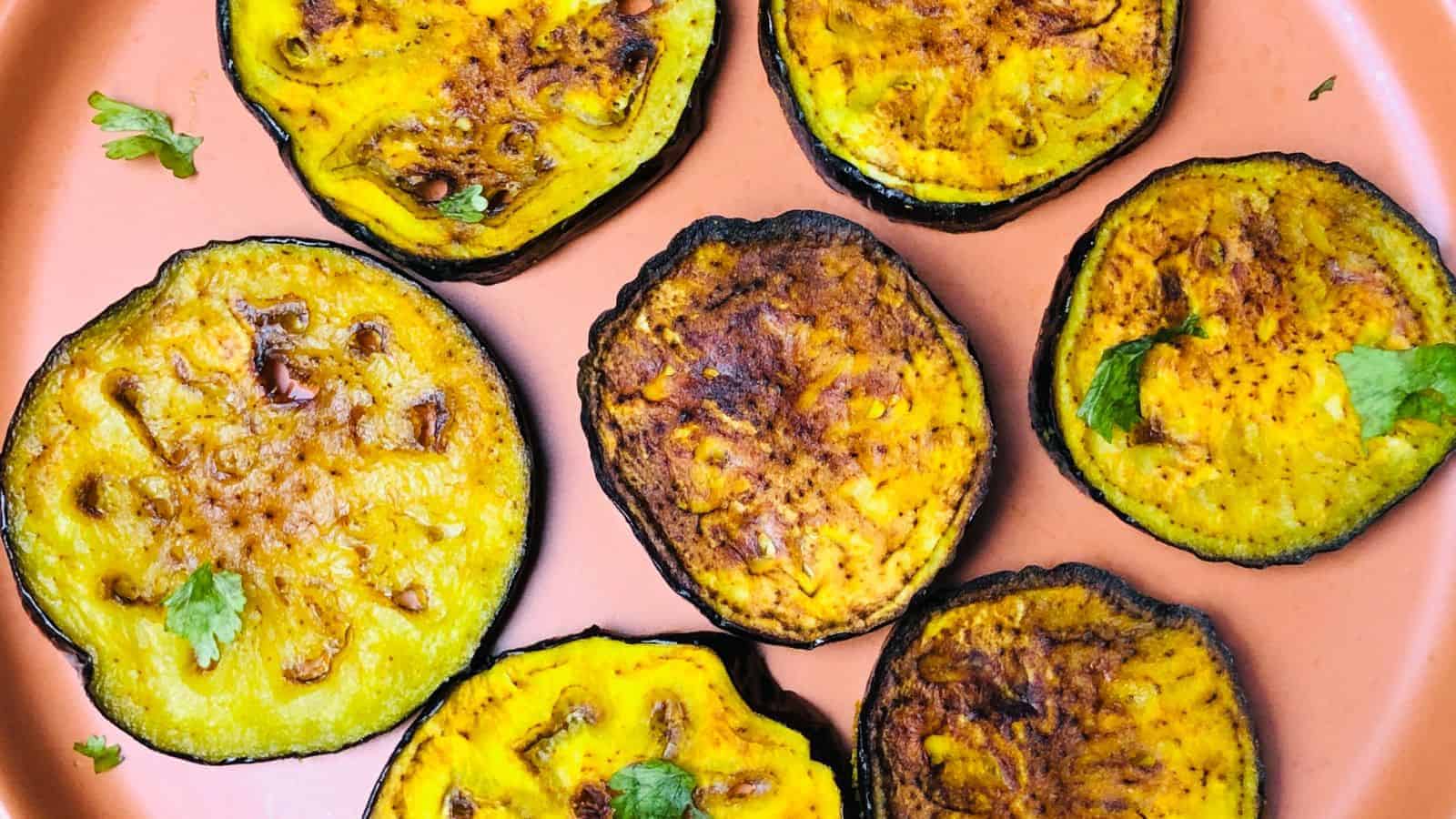 Slices of grilled eggplant with charred edges on a pink plate, garnished with small cilantro leaves.