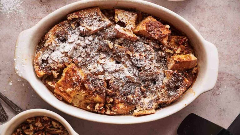 A baked dish of bread pudding topped with powdered sugar and chopped nuts in an oval baking dish.