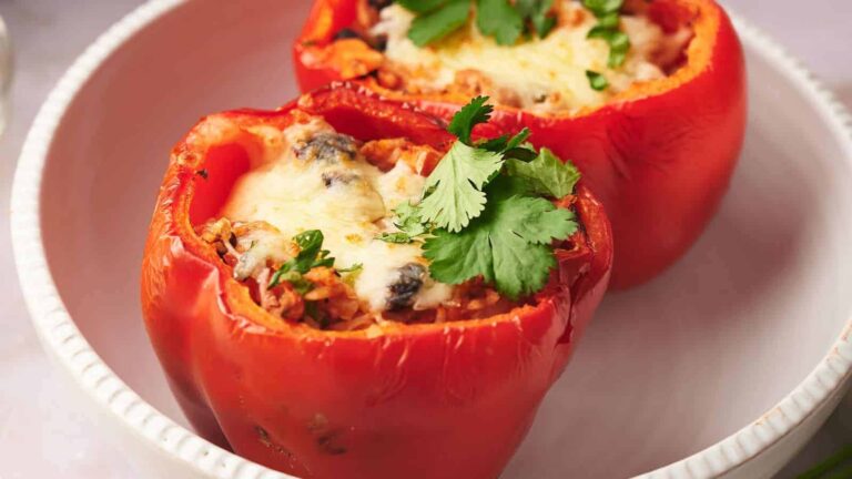 Two stuffed red bell peppers topped with melted cheese and garnished with cilantro in a white dish.