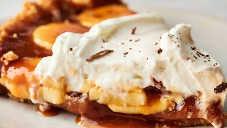 A slice of banoffee pie with bananas, caramel, and a layer of whipped cream, topped with chocolate shavings.