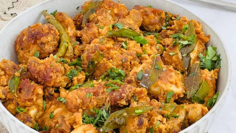 A bowl of fried chicken pieces garnished with green herbs and chili peppers.