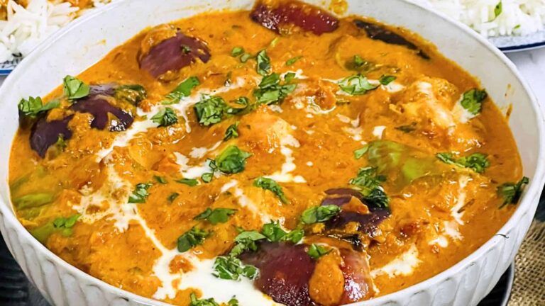 A bowl of curry with purple eggplants, garnished with fresh green herbs and a drizzle of cream.
