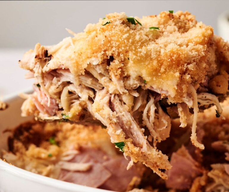 A close-up of a serving of baked Chicken Cordon Bleu casserole topped with breadcrumbs and herbs, being lifted from a dish.