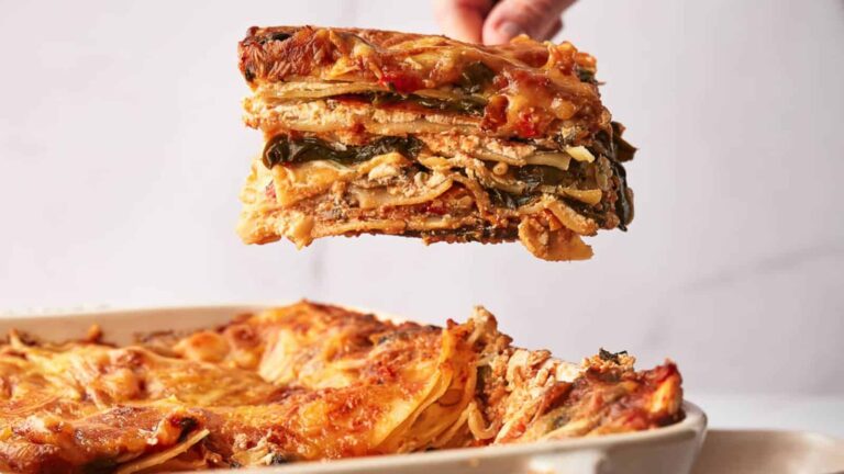 A slice of layered vegetable lasagna is being lifted from a baking dish filled with the same lasagna.