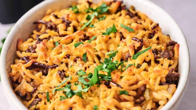 A dish of baked macaroni and cheese with ground beef, topped with chopped parsley.